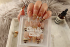 Close up of Golden Bangle 3D gold bangle rings and crystal rhinestones on sheer nude peachy-pink press on nails