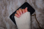 short square french tip nails. press on nails New Zealand. A hand with long, French tip nails rests on a black quilted wallet, draped over a fluffy white blanket.