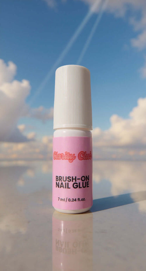 super strong brush on nail glue. Brush-on nail glue in a white bottle with a pink label, 7 ml size, set against a blue sky background.