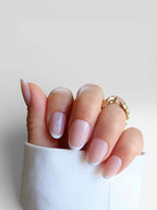 minimal white french tip. short nails. salon quality premier press onsLa Parisienne manicure featuring light pink nails with white tips, hand adorned with a gold ring against a white background.