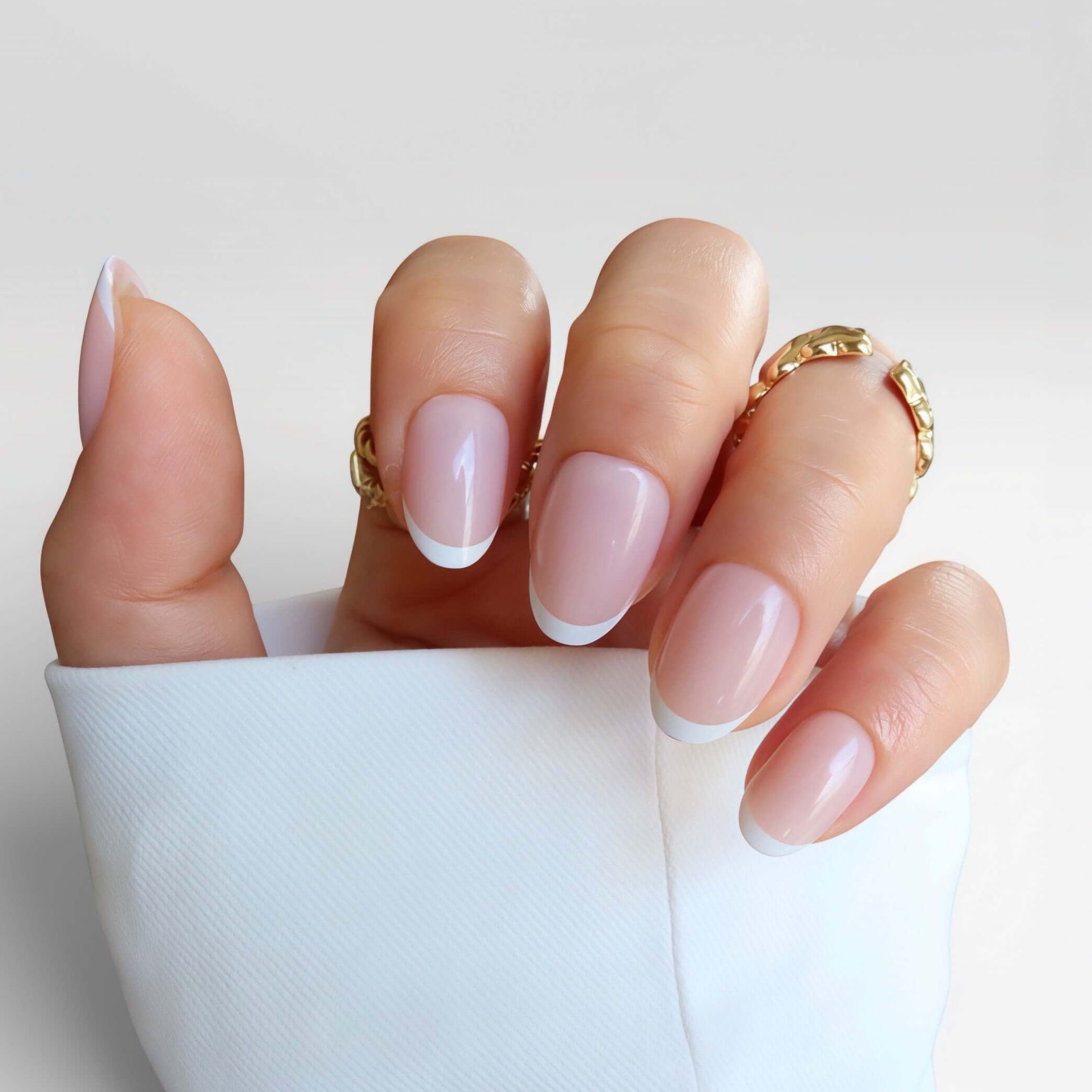 minimal white french tip. short nails. salon quality premier press ons new zealandLa Parisienne nail design featuring a natural pink base with white tips, hand adorned with gold rings on a white background.