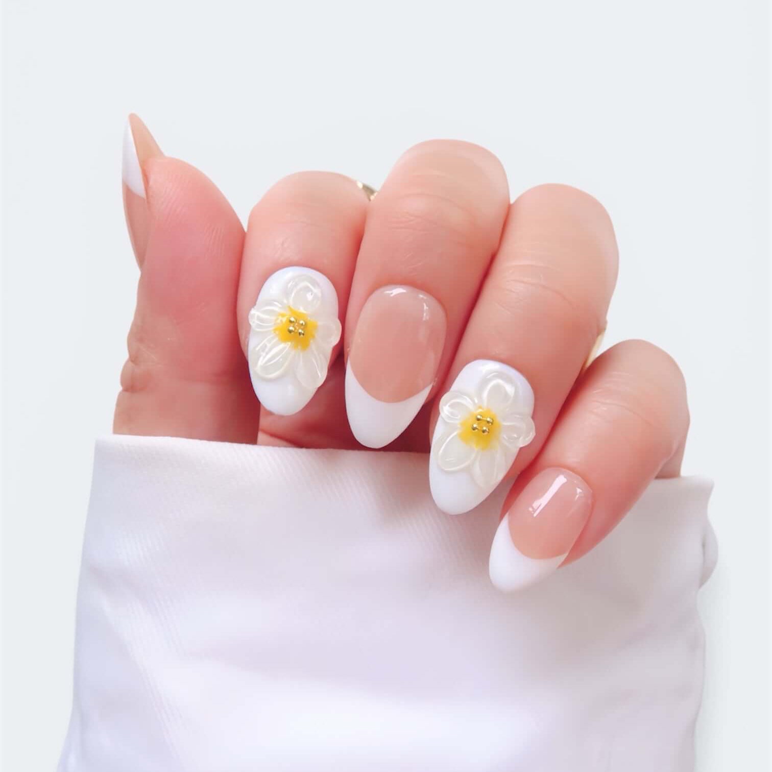 Short almond nails featuring white floral designs with yellow centers on a light background.