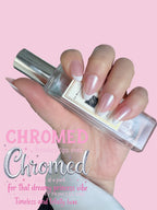 Hand holding a bottle of nail polish with 'Chromed' branding on a pink background