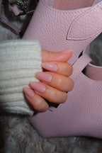 Close-up of a hand with pink nail polish holding a pink shoe. bubble bath neutral nails salon grade durable long lasting press on nails 